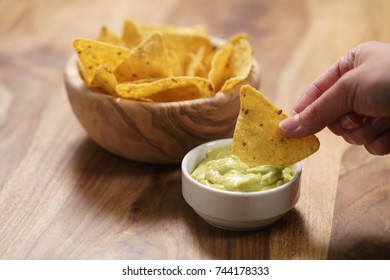 Young Female Hand Dipping Nachos In Guacamole Sauce