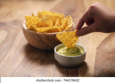 Young Female Hand Dipping Nachos In Guacamole Sauce