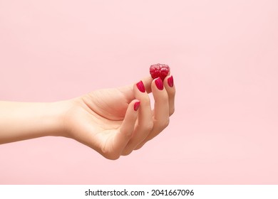 Young female hand hold ripe red raspberry on fingers. Female hand with raspberry isolated on pink background. Female hand with crimson manicure. Crimson nail design.