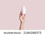 Young female hand holding blank white squeeze bottle plastic tube on pink background. Packaging for pill, capsule or supplement. Product branding mockup. High quality photo