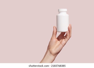 Young female hand holding blank white squeeze bottle plastic tube on pink background. Mockup. High quality photo