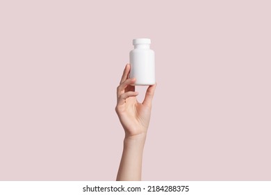Young female hand holding blank white squeeze bottle plastic tube on pink background. Packaging for pill, capsule or supplement. Product branding mockup. High quality photo