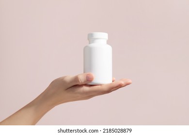 Young female hand holding blank white squeeze bottle plastic tube on pink background. Mockup. High quality photo