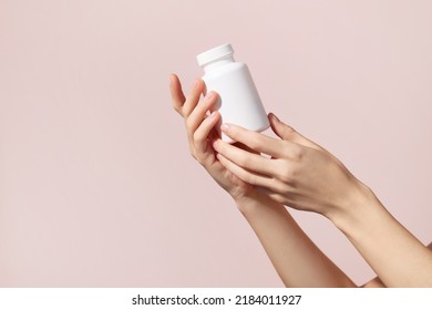 Young female hands holding blank white squeeze bottle plastic tube on pink background. Packaging for pills, capsules or supplements. Mockup. High quality photo