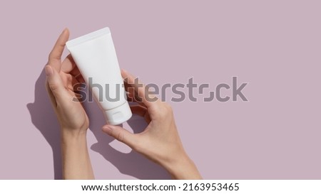 Young female hands holding blank white squeeze bottle plastic tube on pink background. Packaging of cream, lotion, gel, facial foam or skincare. Cosmetic beauty product branding mockup. Copy space. 