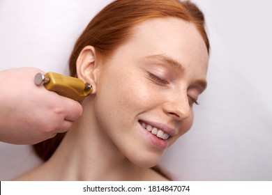 Young Female Having Ear Piercing Process With Special Piercing Gun, Redhead Woman Stand With Closed Eyes, In Beauty Center