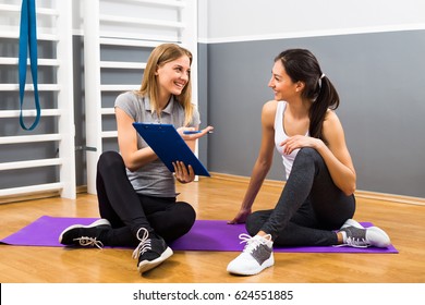 Young Female And Her Fitness Instructor Are Having Conversation At The Gym About Exercising.Woman And Personal Trainer Talking