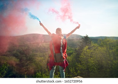 Young Female Hiker Sending Colorful Smoke Signal To Mountaineers