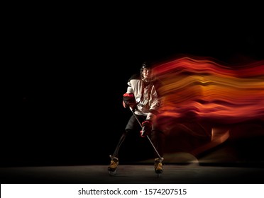 Young female hockey player with the stick on black background and neon light. Sportswoman wearing equipment and helmet practicing. Concept of sport, healthy lifestyle, motion, movement, action.