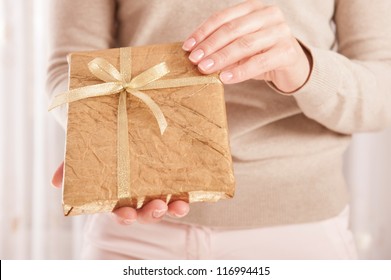 Young female holding a book wrapped in golden paper with ribbon bow