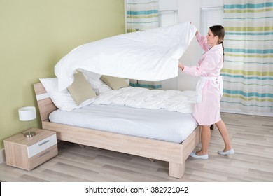 Young Female Housekeeper Changing Bedsheet On Bed In Room