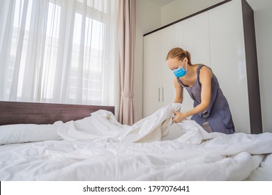 Young Female Housekeeper Wearing A Medical Mask Due To Coronavirus Quarantine COVID 19 Changing Bedding In Hotel Room