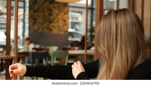 Young female indoors collect and remove dust, lint and fluff from clothes sleeve. Side middle view of a woman with long brown hair in public place with blurred background. High quality 4k footage