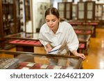 Young female with information brochure looking at the exposition of antique books at historic museum