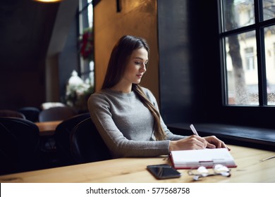 Young Female International Student  Doing Homework Learning New Words From Self-made Vocabulary Preparing For Language Test To Continue Education In University Sitting In Quiet Library Near Window 