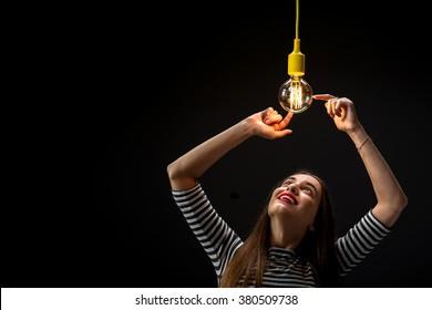 Young Female Inventor Looking On The Illuminated Retro Lamp On The Dark Background