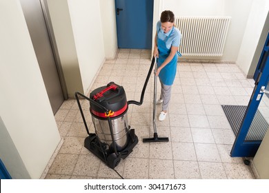 Young Female Janitor Cleaning Floor With Vacuum Cleaner