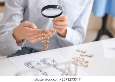 Joven diseñador de joyería femenina con lupa examinando pulsera en taller, primer plano