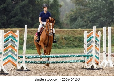 Young Female Jockey On Horse Leaping Over Hurdle.