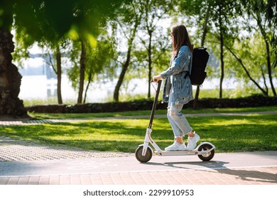 Young female legs on an electric scooter. Beautiful woman rides an electric scooter in the park on a sunny day. Ecological transport. Active lifestyle.