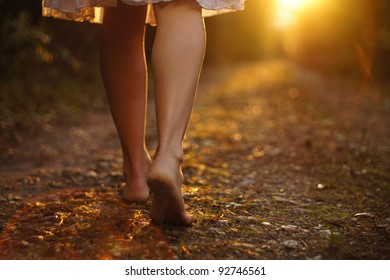 Young female legs walking towards the sunset on a dirt road
