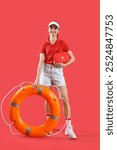 Young female lifeguard in cap with rescue ring and first aid kit on red background