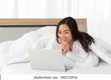 Young Female Lying On Bed Using Notebook Computer. Happy Female Using Laptop At Home In Bedroom. Working From Home In Quarantine Lockdown. Women Watching Movie On Laptop Lying In Bed.