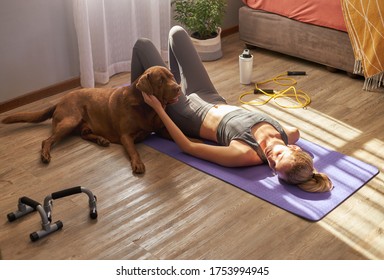 Young female lying on mat after workout at home with dog in the morning sun. - Powered by Shutterstock