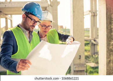 Young female and male engineers or business partners cooperating on floor plans on a construction site. Architecture and teamwork concept.
