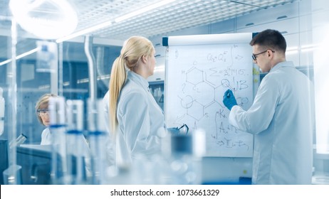 Young Female And Male Scientists Write Formulas On A Whiteboard. They're Solving Scientific Problems In Bright Modern High Tech Laboratory.