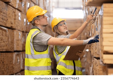 Young female and male workers in a factory for the production of furniture, wood factory. Inspecter factory worker holding clipboard checking quality of wooden products at import export wood warehouse