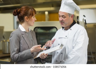 Young female manager talking to the head cook standing in a professional kitchen