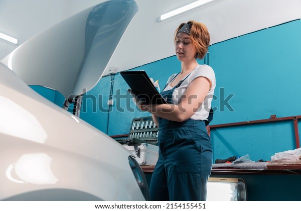 Young female mechanic checks documents of order\
to service for car. Bottom view. The concept of women\'s equality\
and workshop.