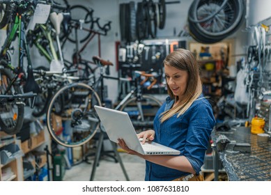 Young female mechanic with laptop. Business woman at a factory. Woman mechanic working on a laptop. Female Bicycle Mechanic.  - Powered by Shutterstock