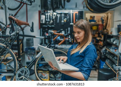 Young female mechanic with laptop. Business woman at a factory. Woman mechanic working on a laptop. Female Bicycle Mechanic.  - Powered by Shutterstock