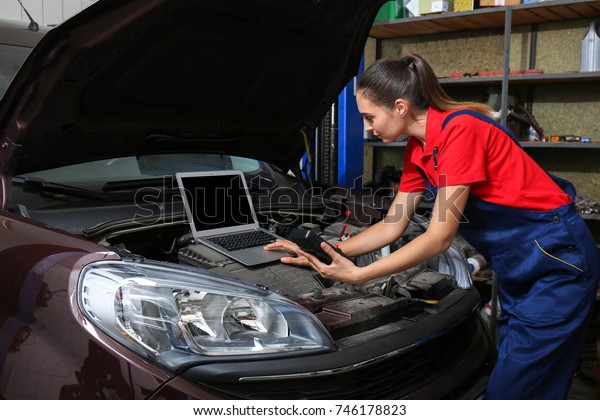 Young female mechanic with laptop repairing car in\
body shop