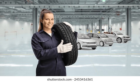 Young female mechanic worker carrying a car tire inside a garage - Powered by Shutterstock