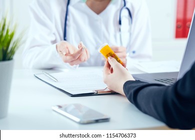 Junge Ärztin, die vor dem Arbeitstisch sitzt und eine Tablette Pillen hält, erklärt dem Patienten, wie er Medikamente einnehmen soll. Konzept der Medizin und Pharmazie