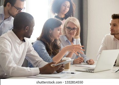 Young female mentor leader coach teaching employees group analyzing online project explaining business strategy speaking training diverse corporate team with laptop using computer at office meeting