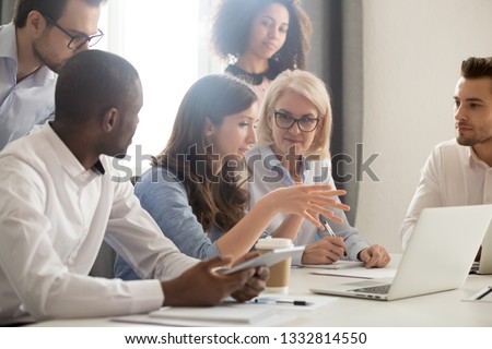 Young female mentor leader coach teaching employees group analyzing online project explaining business strategy speaking training diverse corporate team with laptop using computer at office meeting