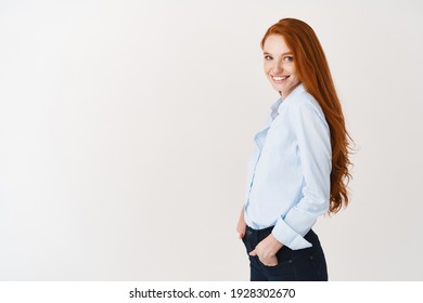 Young Female Model With Ginger Hair And Blue Eyes Turn Head At Camera, Standing In Office Shirt And Smiling, White Background.