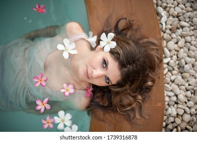 Young Female Model In Hippie, Boho Style. Woman In Swimming Pool With Flowers