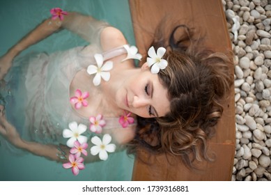 Young Female Model In Hippie, Boho Style. Woman In Swimming Pool With Flowers