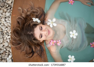 Young Female Model In Hippie, Boho Style. Woman In Swimming Pool With Flowers