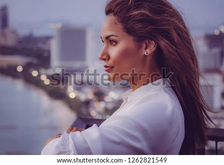 Young female model on a rooftop in Pattaya with beach and city skyline in the back.