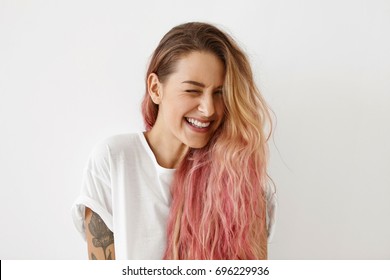Молодая женская модель с розовыми кончиками волос, подмигивая глаза, наслаждаясь радостью, широко улыбаясь, чувствуя радость. Красивая женщина хипстер с длинными волосами чувство счастья во время фотографирования в студии