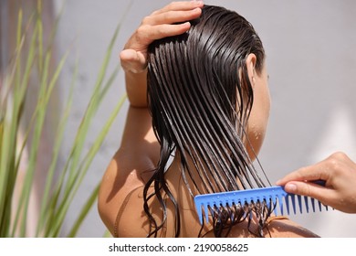 Young Female Model Putting Refreshing Mask On Long Wet Hair With Wooden Comb. Closeup Of Beautiful Woman Hairbrushing With Comb At the Street. Health Care. High Resolution 