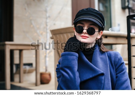 Young female model wearing black baker boy cap and round sunglasses. Outdoors lifestyle portrait