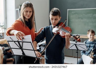 Young female music teacher working with student playing violin at music class at school - Powered by Shutterstock