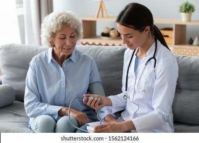 Young female nurse doctor measure high low blood pressure check old woman grandma hypertension sufferer using medical digital electronic tonometer at home, senior people cardiology healthcare concept